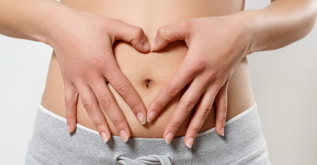 Close-up of a woman’s hands forming a heart shape over her lower abdomen, symbolizing care and awareness for digestive and reproductive health during Food Allergy Week.