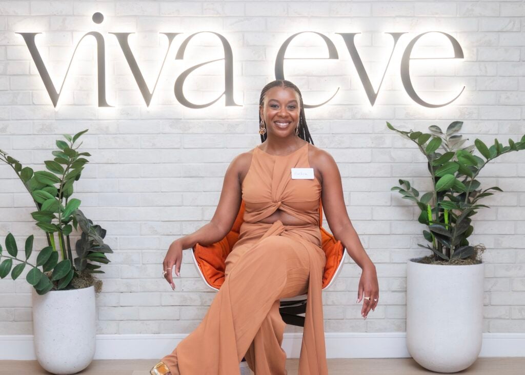 Fibroid patient Ambra Brice seated in front of Viva Eve sign, smiling during her testimonial about learning to trust her body again.