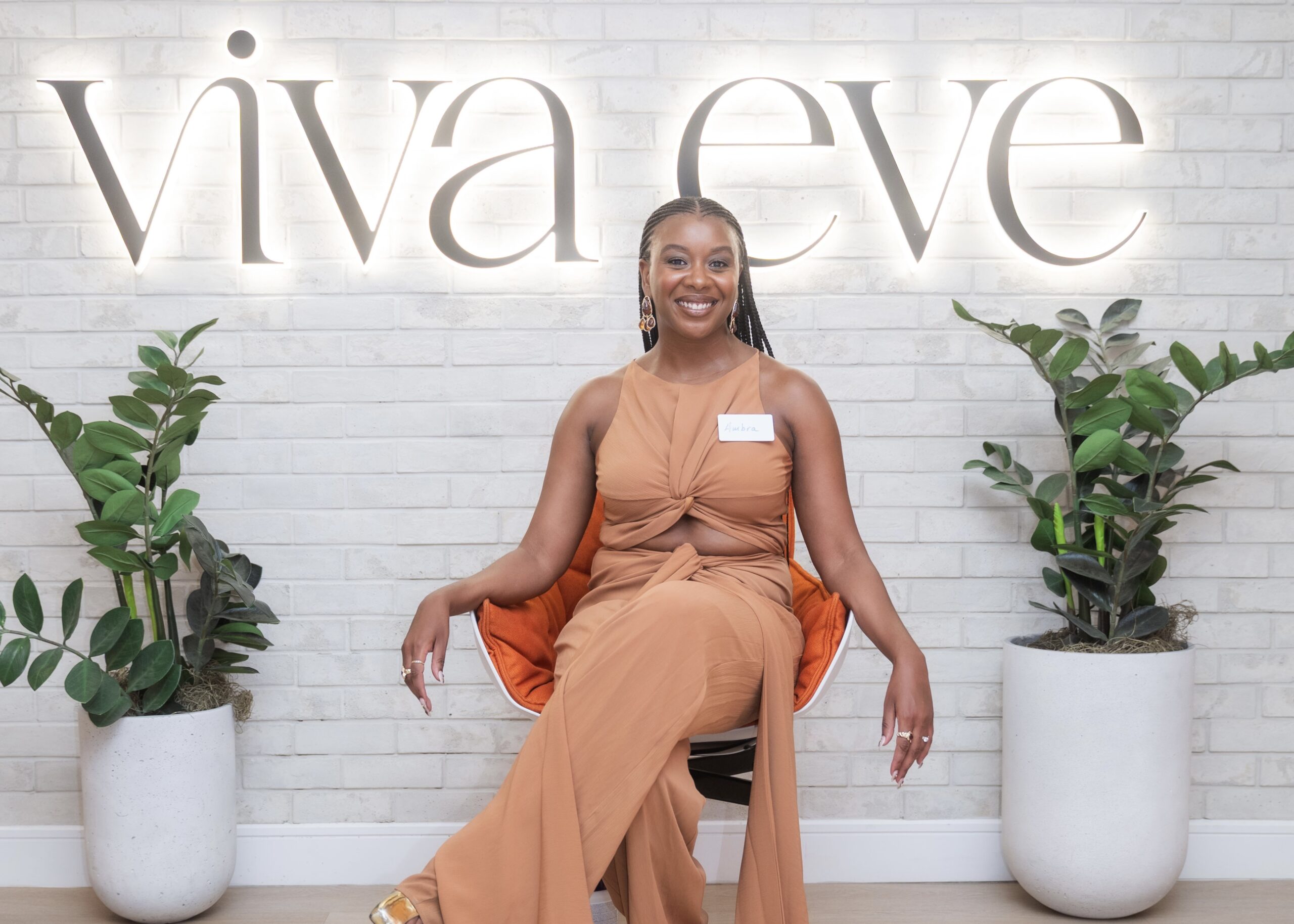 Fibroid patient Ambra Brice seated in front of Viva Eve sign, smiling during her testimonial about learning to trust her body again.