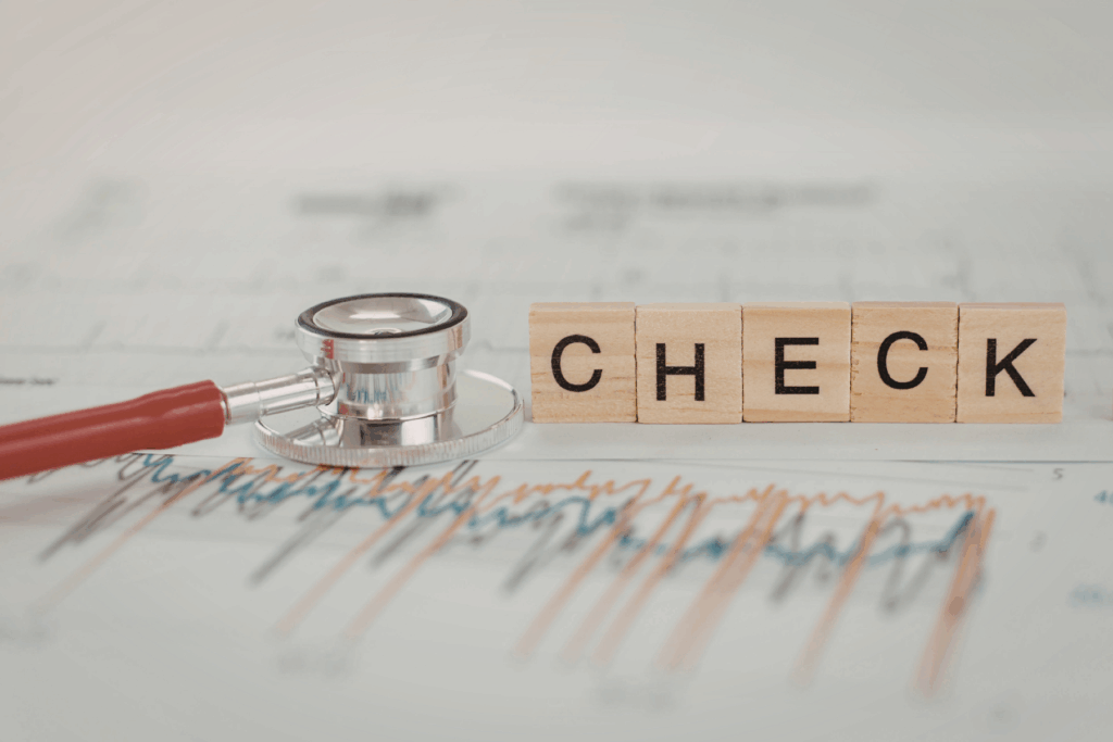 Stethoscope next to wooden blocks spelling ‘check’ on a medical chart, representing medical evaluation and diagnosis.