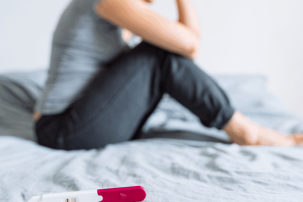 Negative pregnancy test on bed in foreground with woman sitting on bed in background
