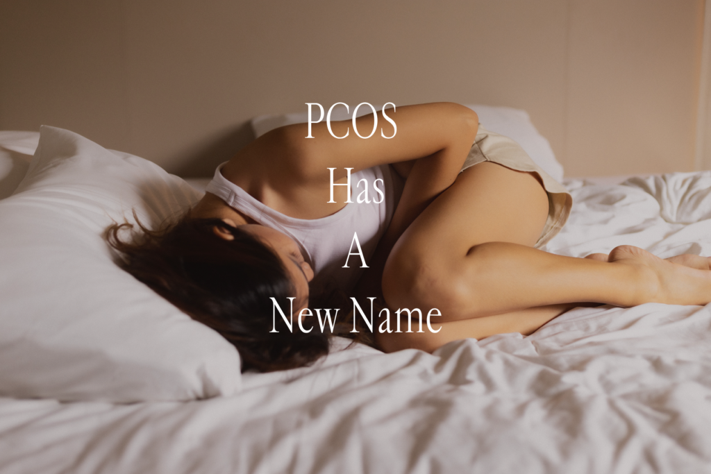 Woman lying in bed holding her abdomen, illustrating the chronic pain and fatigue associated with PCOS symptoms, now being reclassified as PMOS — polyendocrine metabolic ovarian syndrome.